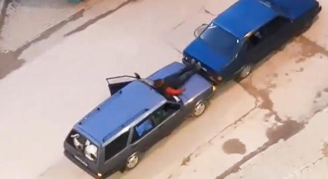 Otomobilin kaputuna oturup, ayaklarıyla öndeki aracı itti